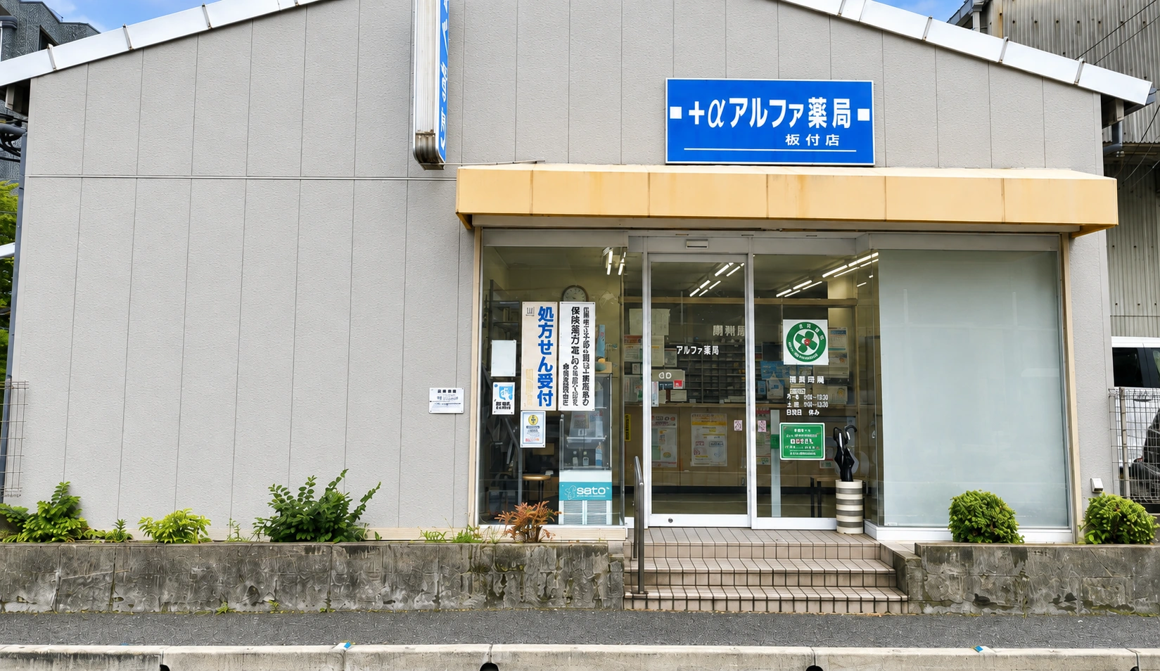 青い看板と黄色いひさしが目印のアルファ薬局板付店の外観